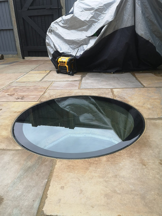 A close-up of the glass well cover's steel support frame, showing it sitting on top of the well and the flooring laid right up to its edge.
