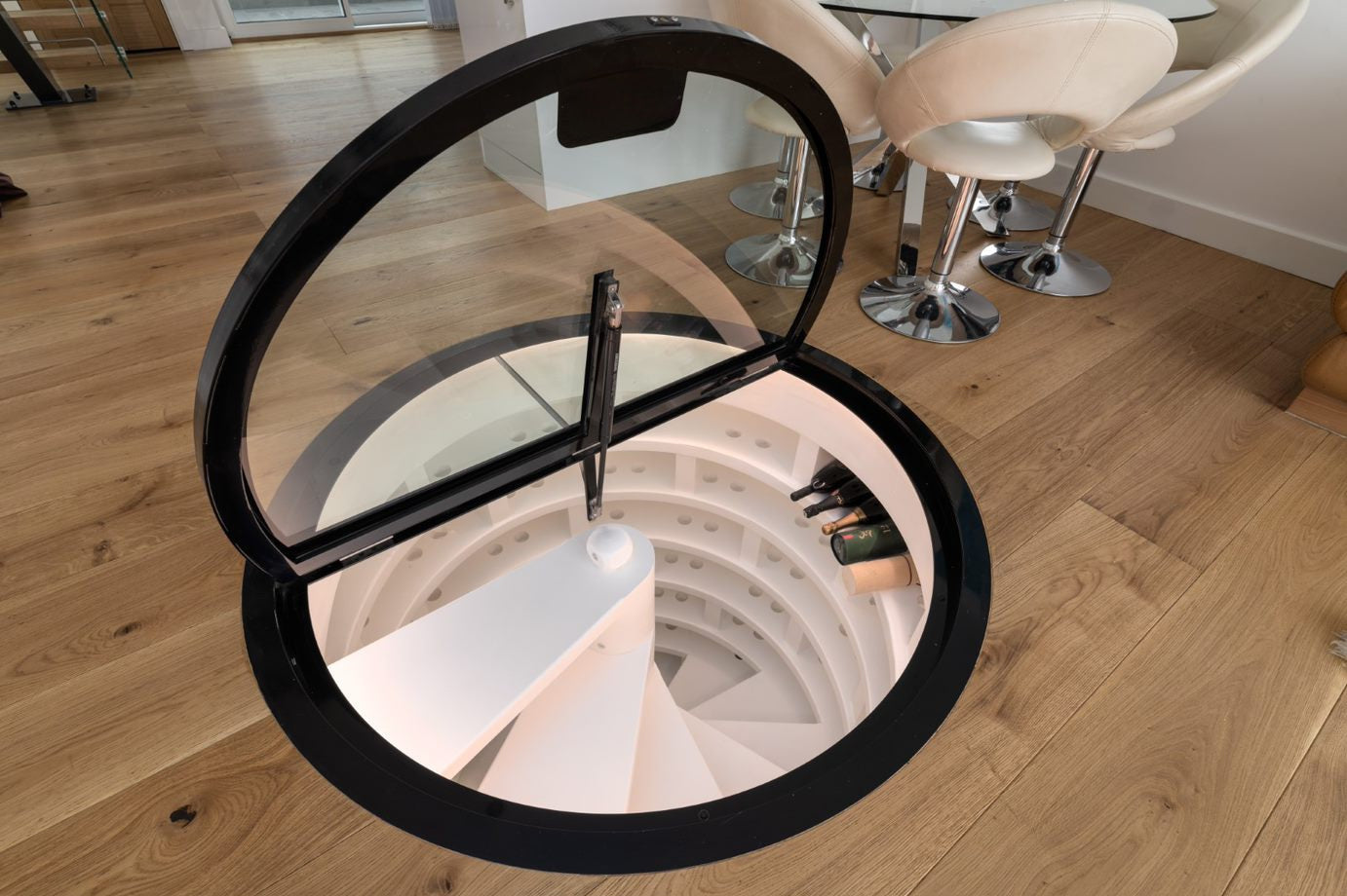 Round glass floor with black metal frame over spiral wine cellar