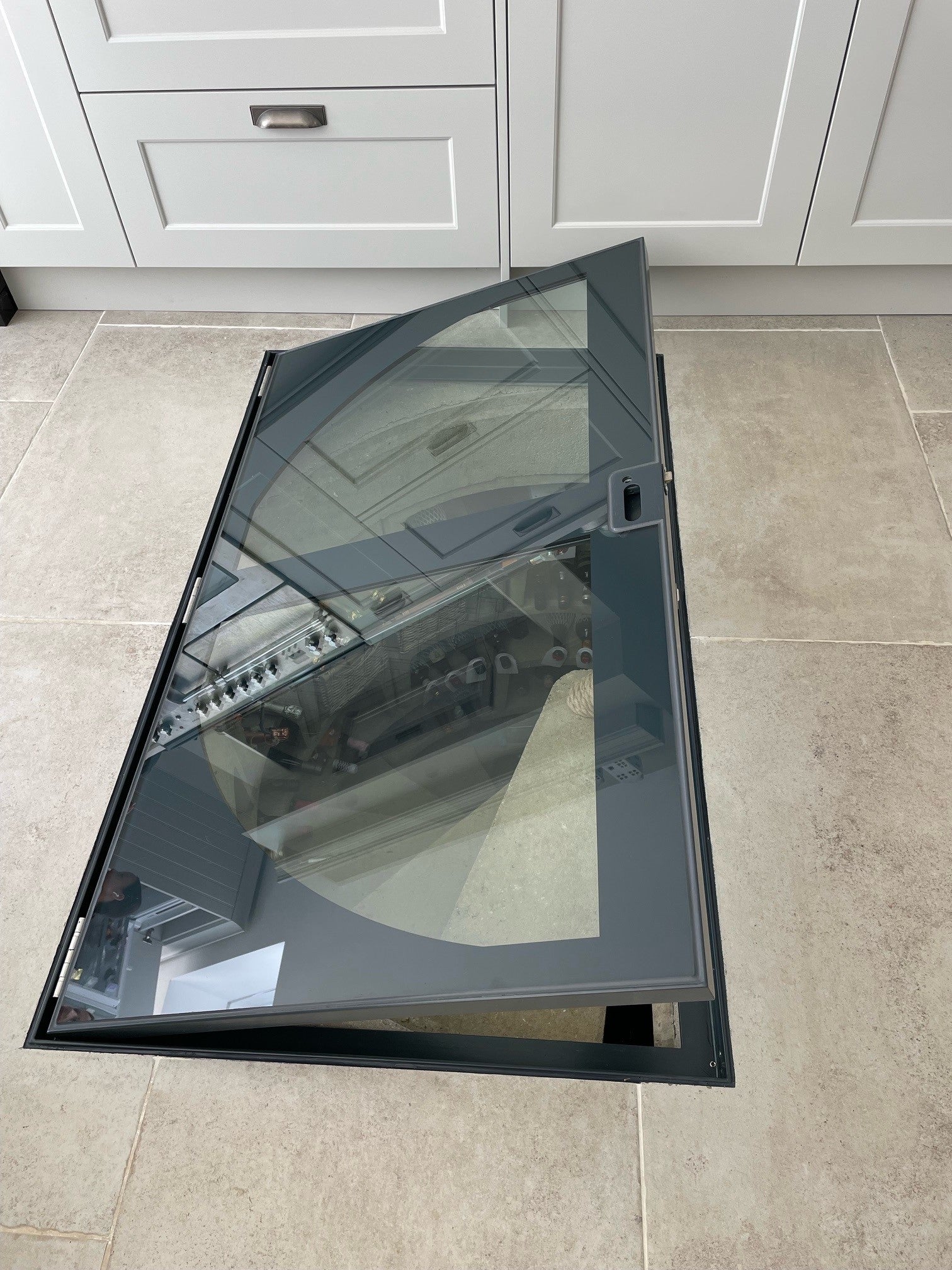 A custom glass wine cellar door seamlessly integrated into a tiled kitchen floor, showcasing the minimalist design and unique painted border.