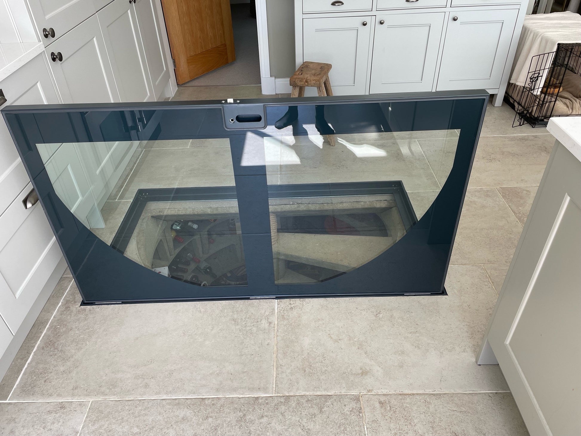 A close-up of a hinged glass wine cellar door handle, showing the secure locking mechanism and sleek powder-coated steel framework.